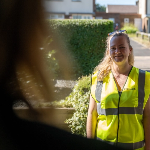 Evermark representative in a branded high-visibility vest speaking with a resident at their home.